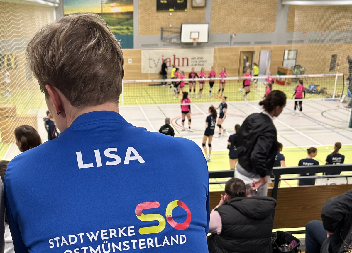 Lisa Thomsen sitzt auf der Tribüne einer Volleyballhalle und beobachtet das Spiel